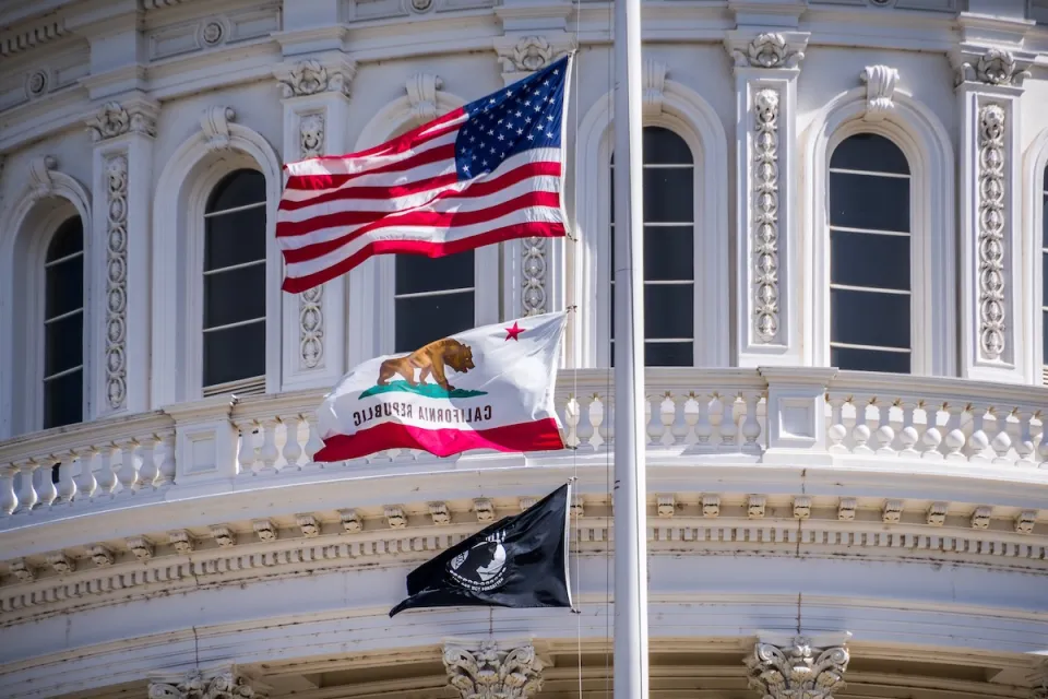 Close-up of U.S., California, and POW-MIA flags on California state capitol dome.